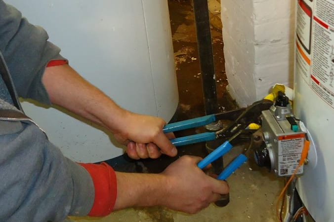 Hands using two pliers to stabilize and tighten a water-heater fitting